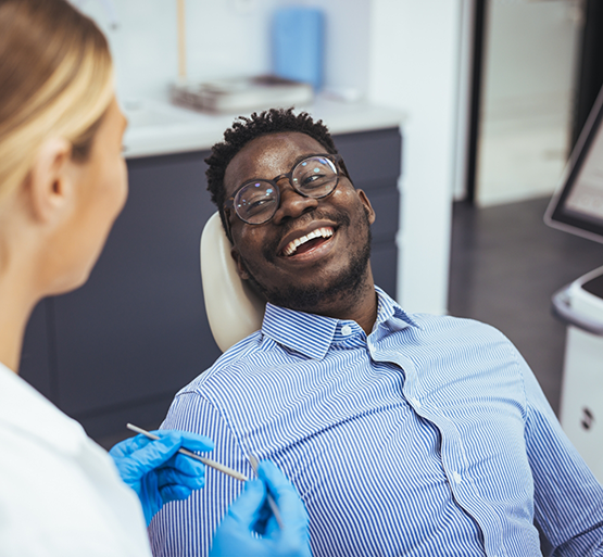 Man with glasses lying back in dental chair and laughing