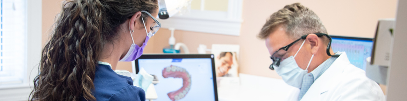 Dentists with masks sitting near monitor with digital impression of teeth