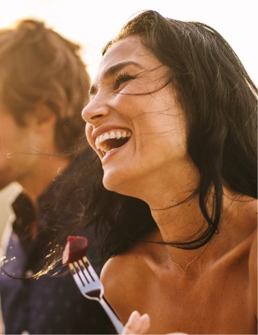 Close up of laughing woman in orange shirt holding a fork